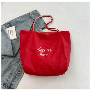 Detail of red canvas tote bag featuring white artistic lettering and striped handles