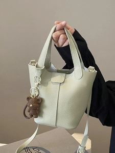 Sage green leather bucket bag with top handle, crossbody strap and woven bear charm