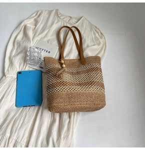 Detail of handwoven striped straw tote with brown leather strap and tassel decoration
