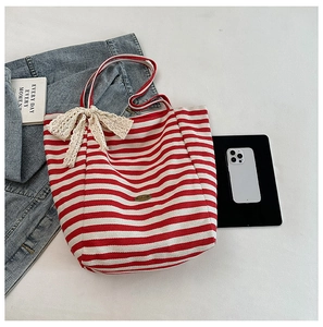 Detail of red striped canvas tote bag featuring cream lace bow and daily essentials