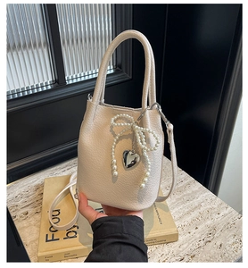 Détail d'un sac seau en cuir crème avec nœud en perles et pendentif cœur argenté