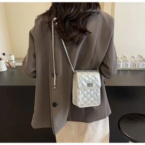 Detailed view of silver quilted crossbody bag with chain strap shown on a model