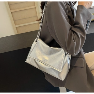 Detail of silver metallic textured shoulder bag with chain strap worn with grey suit