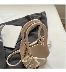 Détail d'un sac seau beige avec pendentif nœud perlé et texture cuir sur surface en tissu