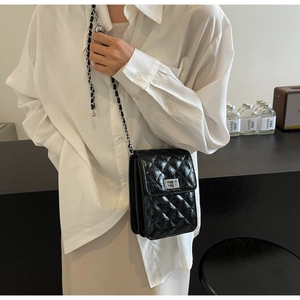 Detail of black quilted crossbody bag with metal chain strap and silver twist-lock closure
