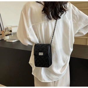 Detail showing a black quilted crossbody bag with a chain strap on a white shirt
