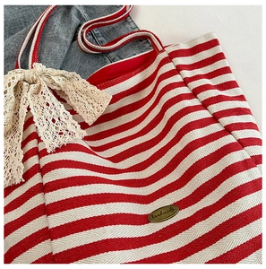 Detail of red and white striped canvas tote bag with lace bow and handmade metal plate