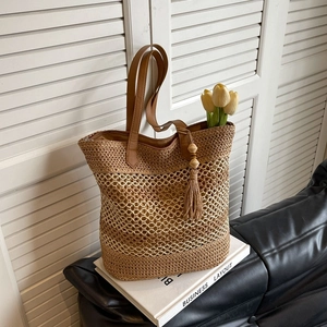 Large woven straw tote bag with brown leather handles and decorative wood bead tassels