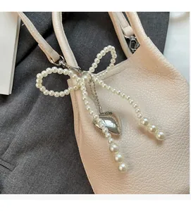 Gros plan d'un bijou de sac avec nœud en perles et cœur argenté sur sac en cuir beige