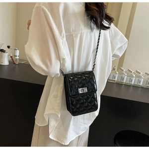 Detail of black quilted crossbody bag with silver chain strap and metal turn lock