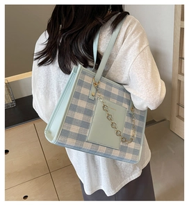 Close-up of blue plaid canvas tote bag with leather pocket and gold flower chain