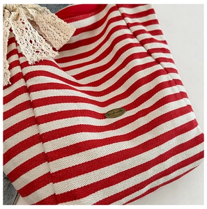 Close-up of red striped canvas tote with handmade metal tag and lace bow detail