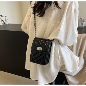 Detail of black quilted leather crossbody bag featuring silver turn-lock and chain strap