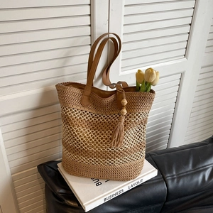 Handwoven straw tote bag with brown leather handles and decorative tassel for beach vacation