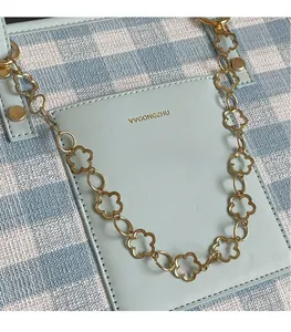 Detail of blue plaid fabric tote with leather pocket and gold floral chain accessory
