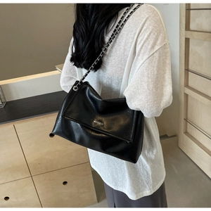Detail of a black textured shoulder bag with silver chain strap and white brand logo