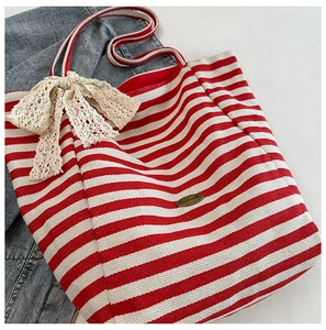 Detail of red striped canvas tote bag with lace bow and handmade metal plate