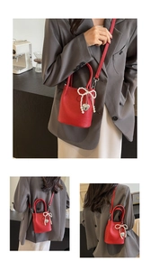 Détail du sac seau rouge à motif litchi avec nœud en perles et pendentif cœur