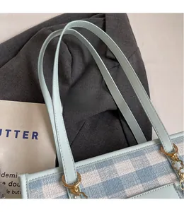 Detail of light blue checkered tote bag featuring golden hardware and clover charm