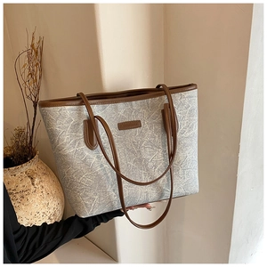 Detail of blue denim tote bag with brown leather handles and brand plaque shown in use
