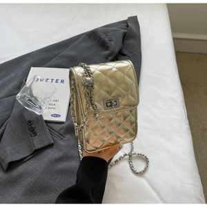 Detail of gold quilted crossbody bag featuring chain strap and metallic twist lock