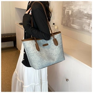 Detail of the light blue pleated tote bag with brown leather handles worn by a model