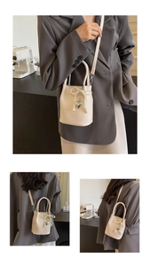 Détail du mini sac seau crème avec décoration de nœud en perles et pendentif cœur argenté