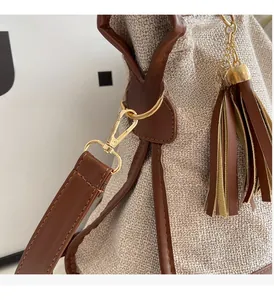 Close-up of gold metal rings and leather tassels on a beige canvas shoulder bag
