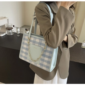 Detail of checkered tote bag featuring blue leather trim and golden flower chain accent