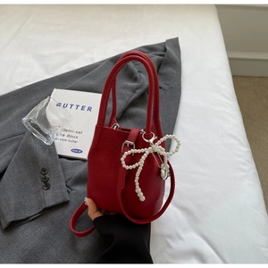 Détail du sac seau en cuir rouge grainé avec breloque nœud en perles et fermoirs argentés