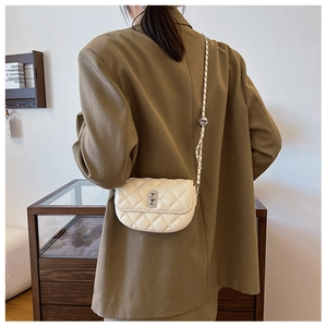 Back view of model wearing a beige quilted saddle bag with silver chain and metal bead