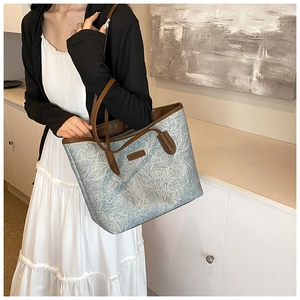 Macro detail of a large textured tote bag featuring brown leather trim and slim shoulder straps