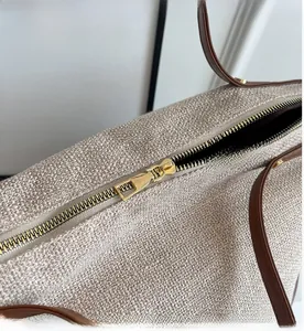 Detailed macro view of the smooth gold metal zipper and brown leather trim on a tote bag