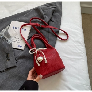 Détail du sac seau rouge en cuir grainé avec nœud en perles et pendentif cœur argenté