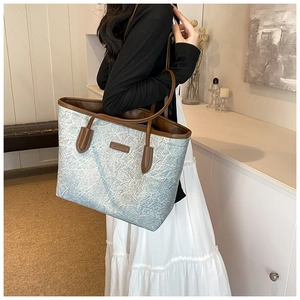 Detail of silver tote bag with brown leather trim and shoulder straps in modern room