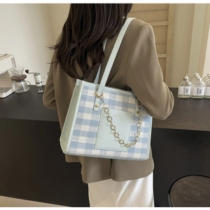 Detail of light blue plaid tote bag featuring a decorative gold flower chain and shoulder strap