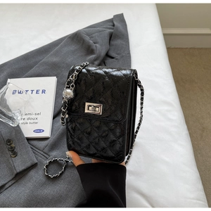 Detail of black quilted crossbody bag with silver chain strap and metal ball decoration