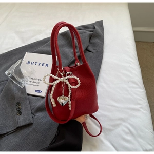 Détail du sac seau rouge en cuir grainé avec nœud en perles et pendentif cœur argenté