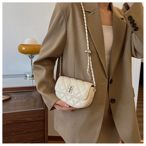Detail of a creamy white quilted crossbody bag with silver chain strap and metal lock
