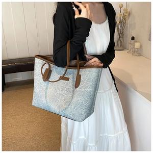 Textured light blue tote bag with brown leather handles worn by a model in a home setting