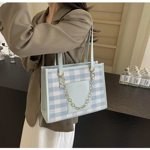 Detail of light blue checkered tote bag with gold flower chain and brand leather patch