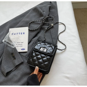 Detail of black quilted leather bag with silver chain strap on a grey suit jacket