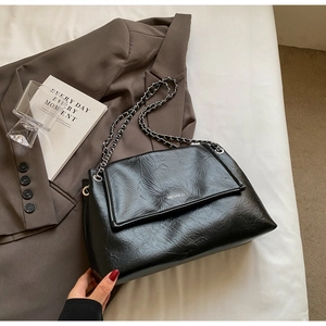 Close-up of black wrinkled leather shoulder bag with silver logo and chain strap