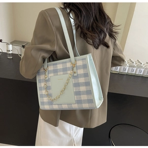 Detail of blue and white checkered tote bag featuring a gold chain and leather handle