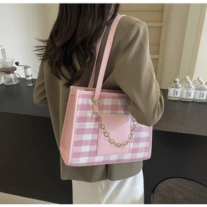 Detail of pink plaid tote bag with leather pocket and golden flower chain on shoulder