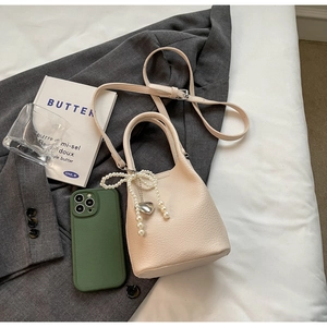 Vue détaillée d'un mini sac seau blanc crème avec nœud en perles et breloque cœur sur veste