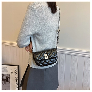 Detail of black quilted leather saddle bag with silver chain strap worn over the shoulder