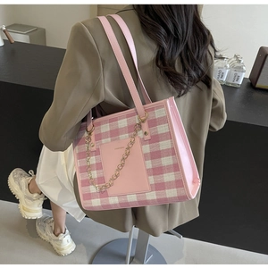 Detail of pink plaid tote bag with golden chain and long handles on a model