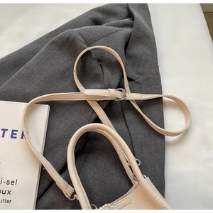 Détail du sac à main beige en cuir grainé avec chaîne en perles sur un costume gris
