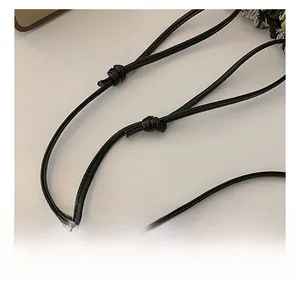 Detail of a slim black leather shoulder strap with a handcrafted knot and fine stitching
